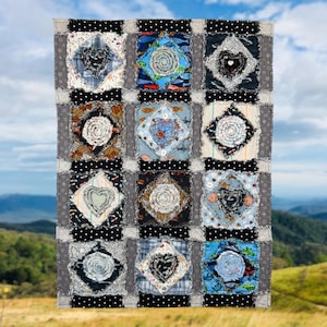 May include: A patchwork quilt with a grid pattern. Each square features a unique design with various fabrics, including floral and heart motifs. The quilt's border is gray with black polka dots, and the background shows a blue sky and green hills.