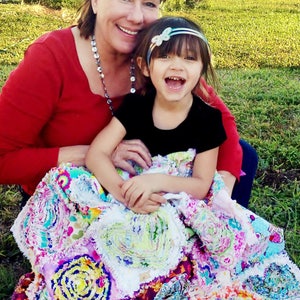 Puede incluir: Una mujer y una ni&ntilde;a peque&ntilde;a est&aacute;n sentadas en una colcha de retazos colorida. La mujer lleva un su&eacute;ter rojo y la ni&ntilde;a lleva una camisa negra. La colcha est&aacute; hecha de muchas telas y colores diferentes.