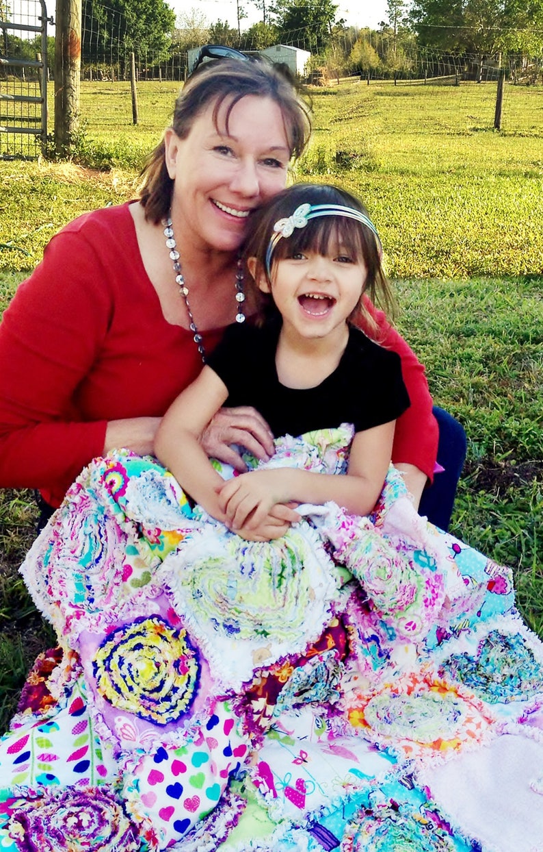 Puede incluir: Una mujer y una ni&ntilde;a peque&ntilde;a est&aacute;n sentadas en una colcha de retazos colorida. La mujer lleva un su&eacute;ter rojo y la ni&ntilde;a lleva una camisa negra. La colcha est&aacute; hecha de muchas telas y colores diferentes.