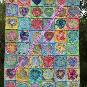 Puede incluir: Una colcha colorida con un dise&ntilde;o de patchwork que presenta varios tonos de amarillo, verde, azul, rosa y rojo. La colcha est&aacute; hecha de cuadrados con diferentes patrones, incluyendo corazones, remolinos y lunares. El texto "Summer in the Park &copy; by ItssewSally Etsy" est&aacute; escrito en rosa en la colcha.