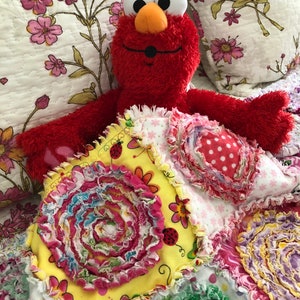 Puede incluir: Un peluche rojo de Elmo est&aacute; acostado sobre una colcha de retazos colorida hecha a mano. La colcha est&aacute; hecha de varias telas con diferentes patrones y texturas, incluyendo flores, lunares y remolinos. La colcha es una adici&oacute;n brillante y alegre a la habitaci&oacute;n de cualquier ni&ntilde;o.