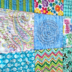 Puede incluir: Una colcha de retazos con una variedad de telas y patrones coloridos, incluyendo dise&ntilde;os florales, paisley y geom&eacute;tricos. La colcha est&aacute; acolchada con una forma de coraz&oacute;n en el centro de cada cuadrado.