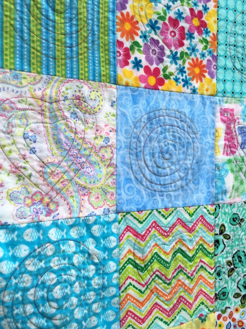 Puede incluir: Una colcha de retazos con una variedad de telas y patrones coloridos, incluyendo dise&ntilde;os florales, paisley y geom&eacute;tricos. La colcha est&aacute; acolchada con una forma de coraz&oacute;n en el centro de cada cuadrado.