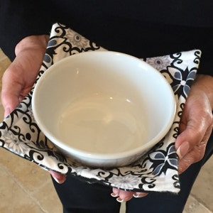 May include: A white ceramic bowl with a black and white floral print fabric bowl cozy.