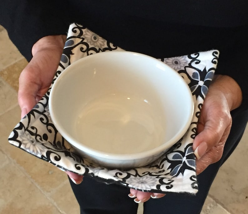 May include: A white ceramic bowl with a black and white floral print fabric bowl cozy.
