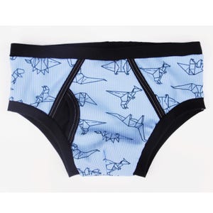 Puede incluir: Ropa interior azul claro con textura acanalada y cintura negra. La ropa interior presenta un estampado de dinosaurios de origami en azul oscuro. Los bordes están ribeteados con tela negra.