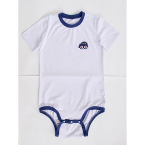 May include: White short-sleeved bodysuit with a blue trim around the neckline and leg openings. The bodysuit has a blue car applique on the front.
