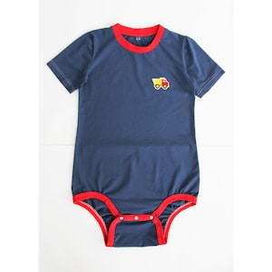 Puede incluir: Body de bebé azul marino con ribetes rojos en el cuello y las piernas. Un pequeño camión amarillo y rojo bordado está en el pecho. El body tiene mangas cortas y corchetes en la parte inferior.