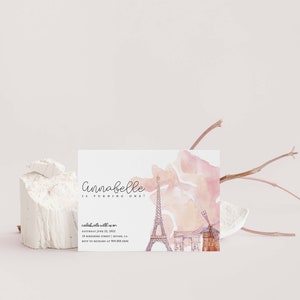 May include: A pink and white watercolor invitation with a Parisian theme. The invitation says "Annabelle is turning one!" and includes a watercolor illustration of the Eiffel Tower, Arc de Triomphe, and a windmill.