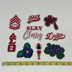 May include: A collection of embroidered patches in red, white, and green. The patches feature text and symbols, including "1913", "SLAY", "Classy", and "Delta". A measuring tape is included for scale.