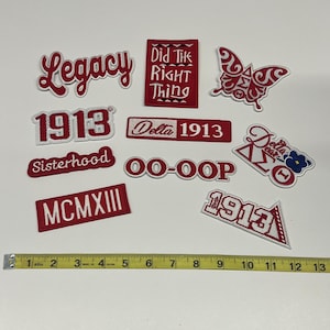 May include: A collection of red and white embroidered patches with various designs and text, including "Legacy," "1913," and a butterfly. A yellow measuring tape is placed below the patches, showing inches.