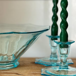 May include: A light blue glass bowl with a scalloped rim and two matching light blue glass candle holders, each containing a tall, dark green spiral-shaped taper candle. The items feature a translucent finish and a smooth, reflective surface.