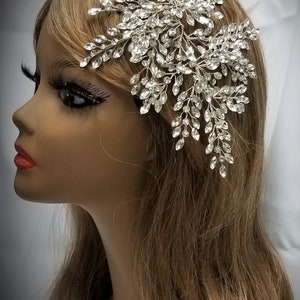 May include: A silver bridal hair comb with a large, intricate design of crystal leaves and branches. The comb is perfect for adding a touch of sparkle to any bridal hairstyle.