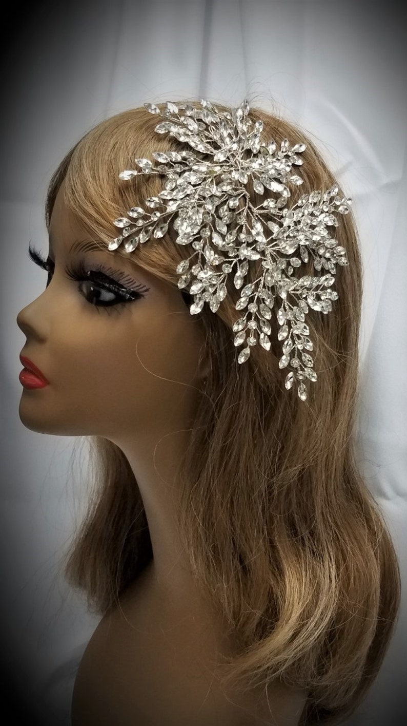 May include: A silver bridal hair comb with a large, intricate design of crystal leaves and branches. The comb is perfect for adding a touch of sparkle to any bridal hairstyle.