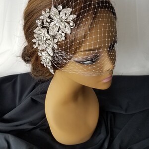 Puede incluir: Un velo de novia blanco con un peine de pelo floral de pedrer&iacute;a plateada. El velo est&aacute; hecho de un material de malla fina y el peine est&aacute; adornado con pedrer&iacute;a brillante.