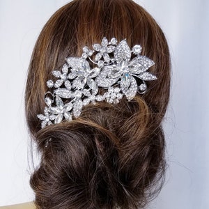 Puede incluir: Peine de pelo plateado con un dise&ntilde;o floral con brillantes transparentes. El peine se lleva en el pelo de una mujer.