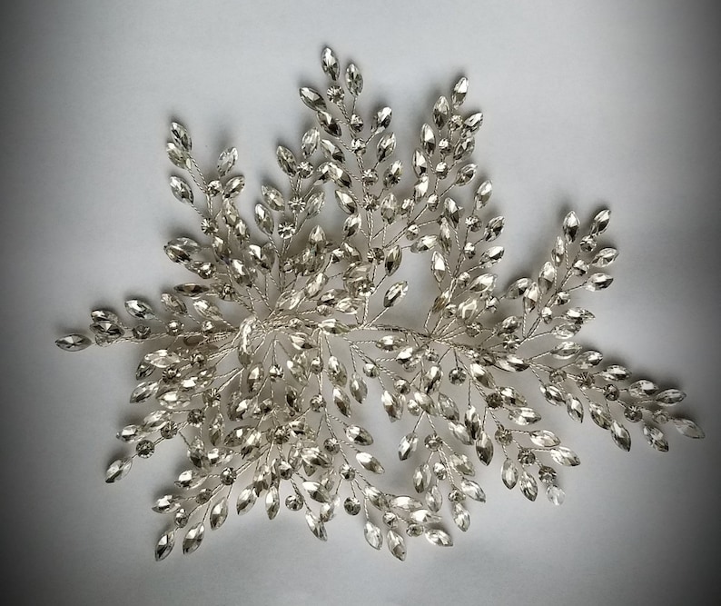 May include: Silver bridal hair comb with a delicate design of crystal leaves and branches. The comb is perfect for adding a touch of sparkle to any hairstyle.