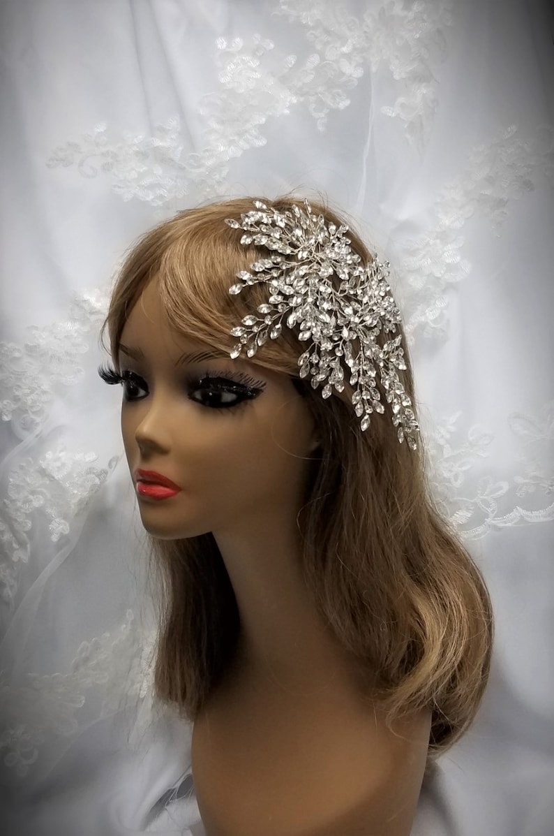 May include: A silver bridal hair comb with crystal rhinestones. The comb is designed in a cascading, floral pattern.