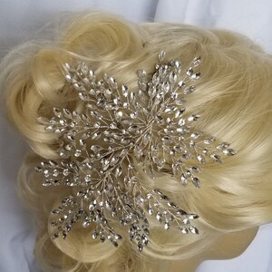 May include: A silver hair comb with crystal embellishments in a floral design. The comb is worn in a blonde updo.
