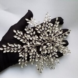 May include: A silver bridal hair comb with a delicate design of crystal leaves and branches. The comb is perfect for adding a touch of sparkle to any wedding hairstyle.