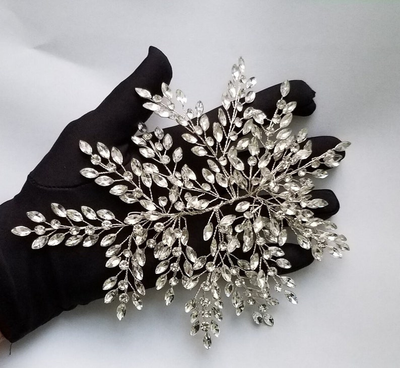 May include: A silver bridal hair comb with a delicate design of crystal leaves and branches. The comb is perfect for adding a touch of sparkle to any wedding hairstyle.