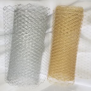 Puede incluir: Dos rollos de tejido de red, uno plateado y otro dorado. La red es una malla fina con un acabado brillante.