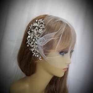 Puede incluir: Un peine de pelo de novia plateado con un dise&ntilde;o floral con brillantes de cristal transparentes. El peine se lleva en el pelo de un maniqu&iacute; con un velo de tul blanco.