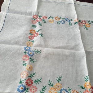 May include: White linen tablecloth with a floral embroidered border. The embroidery features small flowers in shades of pink, yellow, blue, and green.