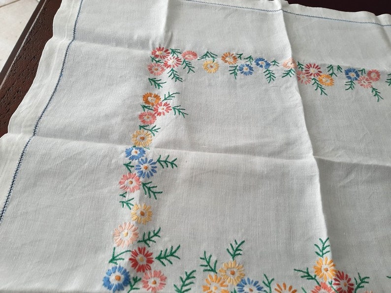 May include: White linen tablecloth with a floral embroidered border. The embroidery features small flowers in shades of pink, yellow, blue, and green.