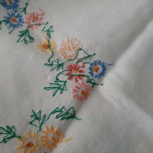 May include: White fabric with embroidered flowers in shades of pink, blue, yellow, and green.