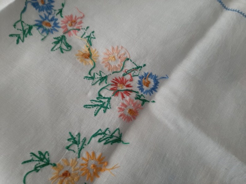 May include: White fabric with embroidered flowers in shades of pink, blue, yellow, and green.