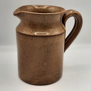 Peut inclure: Une cruche en céramique marron avec une anse et un bec verseur. La cruche a une texture tachetée et une bande légèrement plus foncée au milieu. Conçue pour servir des boissons.