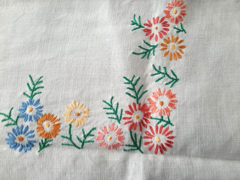 May include: White linen tablecloth with embroidered floral designs in shades of blue, orange, pink, and green.