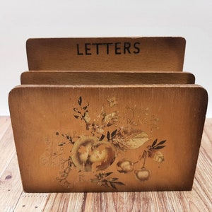 Puede incluir: Un portacartas de madera con la palabra "LETTERS" impresa en la parte superior. El portacartas tiene un diseño floral con detalles dorados y está pintado en tonos marrones.