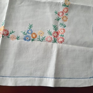 May include: White linen tablecloth with embroidered floral border in shades of blue, pink, and orange.