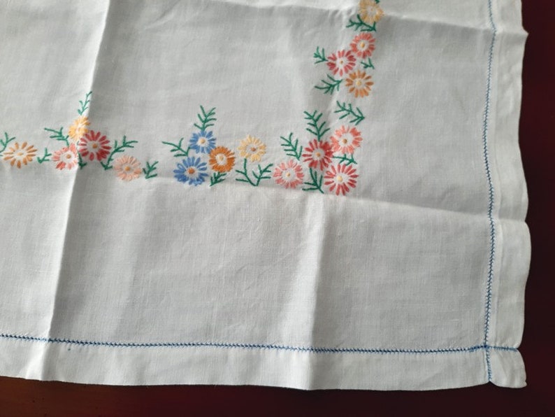 May include: White linen tablecloth with embroidered floral border in shades of blue, pink, and orange.