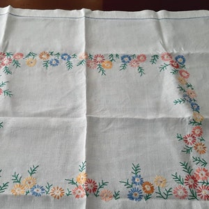May include: White linen tablecloth with a delicate floral embroidery design in shades of pink, blue, and yellow. The embroidery features a repeating pattern of small flowers and leaves around the border.