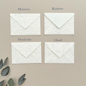May include: Four white envelopes with textured surfaces arranged in a grid. Each envelope features a distinct embossed pattern labeled with text: Monstera, Rainbow, Floral vine, and Cloud. The envelopes have a triangular flap and a rough, organic finish.