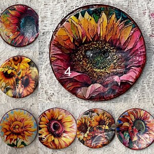 May include: Seven circular decorative items, each featuring a sunflower design. The sunflowers are rendered in various artistic styles, with colours including yellow, orange, red, and green. Each design is numbered from 1 to 7.