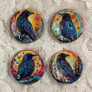 Puede incluir: Cuatro botones redondos de madera con diseños pintados coloridos que presentan un cuervo negro en cada botón. Los botones están numerados del 1 al 4.