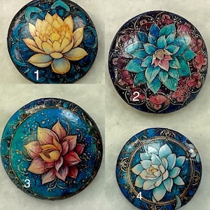 Peut inclure: Quatre sous-verres ronds décoratifs avec un fond bleu et des motifs dorés complexes. Chaque sous-verre présente une fleur de lotus de couleur différente au centre. Les sous-verres sont numérotés de 1 à 4.