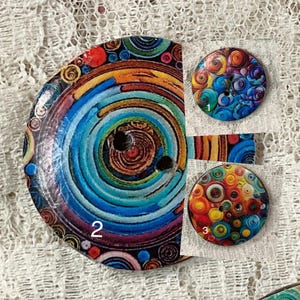 Puede incluir: Tres botones redondos coloridos con diferentes patrones. El primer botón tiene un patrón de espiral azul, naranja y rojo. El segundo botón tiene un patrón de espiral azul, morado y rosa. El tercer botón tiene un patrón de círculo amarillo, naranja y rojo.