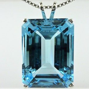 May include: A rectangular, light blue gemstone pendant with a silver chain. The gemstone is a clear, aquamarine color, cut with multiple facets to reflect light. The pendant is suspended from a delicate silver chain, creating a classic jewelry piece.