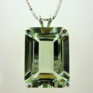 May include: A rectangular, light green gemstone pendant with a silver chain. The gemstone is emerald-cut and set in a silver bezel. The pendant hangs from a delicate silver chain, creating a classic and elegant look. The gemstone has a subtle, translucent quality.