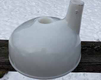 Könnte beinhalten: Ein weißer Keramiktrichter mit rundem Boden und Ausguss. Das Objekt hat eine glatte, glänzende Oberfläche und ein kleines Loch oben am Boden. Der Ausguss erstreckt sich nach oben und zur Seite. Der Trichter befindet sich auf einer Holzoberfläche.