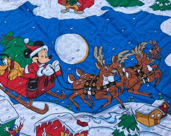 Könnte beinhalten: Ein gesteppter Stoff mit Weihnachtsmotiv, der Mickey Mouse in einem Weihnachtsmannkostüm zeigt, der einen von Rentieren gezogenen Schlitten fährt. Pluto ist im Schlitten. Der Hintergrund ist blau mit Vollmond, Schnee und Zeichentrickhäusern.