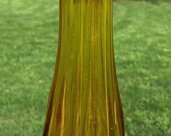 Könnte beinhalten: Eine hohe, bernsteinfarbene Glasvase mit vertikaler Rippenstruktur und einem ausgestellten, gewellten Rand. Der Körper der Vase verjüngt sich von einer breiten, facettierten Basis zu einem schlanken Hals und zeigt einen warmen Farbverlauf.