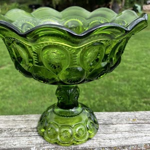 Puede incluir: Un cuenco de cristal verde vibrante sobre pedestal con un borde festoneado y un patrón en relieve de lunas y estrellas que se repite en la superficie exterior. El cuenco se apoya en una base circular resistente que refleja el mismo diseño de cristal texturizado.