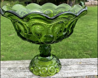 Könnte beinhalten: Eine leuchtend grüne Glasschale auf einem Fuß mit gewelltem Rand und einem sich wiederholenden geprägten Mond- und Sternmuster auf der Außenfläche. Die Schale wird von einem stabilen runden Fuß getragen, der das gleiche strukturierte Glasdesign aufweist.