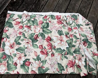 Könnte beinhalten: Blumenstoff mit cremefarbenem Hintergrund, mit großen rosa und weißen Blumen, grünen Blättern und kleineren rosa Blüten. Der Stoff ist gefaltet und zeigt die Wiederholung des Musters. Ideal für Nähprojekte oder Heimdekoration.